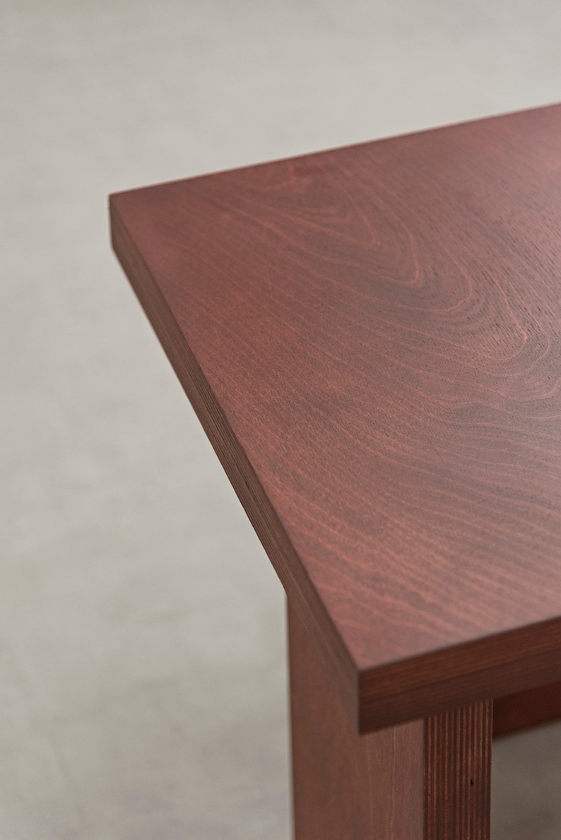 May include: Close-up of the top of a wooden table with a rich reddish-brown finish. The wood grain is visible and the surface is smooth.