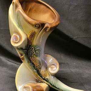 May include: A ceramic vase with an unusual, asymmetrical design. The vase has a brown interior and rim, with a cream and green exterior. Decorative wheat stalks are painted on the side. The vase is approximately 30 cm tall.