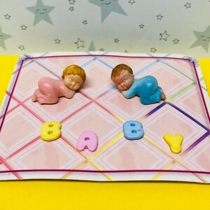 May include: A pink and blue baby figurine set on a pink and white checkered background with the word "BABY" spelled out in colorful letters.