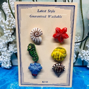 May include: A card with six colorful sea-themed buttons. The buttons are a seashell, starfish, seahorse, fish, coral, and a seashell. The card reads "Latest Style Guaranteed Washable" and "B/10".