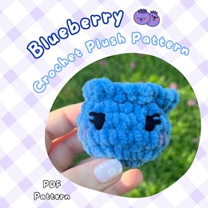 May include: A blue crochet plushie in the shape of a blueberry with black eyes and a smiling mouth. The text "Blueberry Crochet Plush Pattern" and "PDF Pattern" are displayed on a purple and white background.