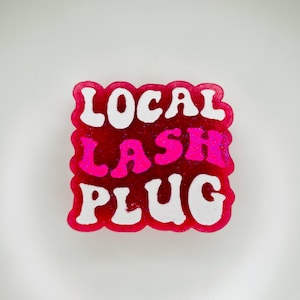 May include: A pink and white resin keychain with the text "LOCAL LASH PLUG" in white letters.