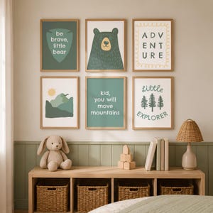 Puede incluir: Un conjunto de seis láminas enmarcadas con ilustraciones de temática natural y texto. Los cuadros incluyen un oso, montañas, pinos y frases como be brave, little bear, adventure y kid, you will move mountains en tonos verdes.