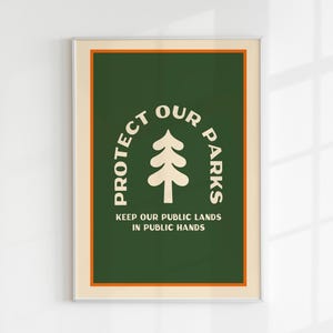 May include: A framed poster with a green background and a cream border. The poster displays the text "PROTECT OUR PARKS" above a stylized tree graphic. Below, it reads "KEEP OUR PUBLIC LANDS IN PUBLIC HANDS". The poster is in a silver frame.