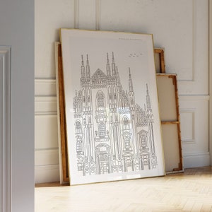 May include: A black and white line drawing of the Duomo di Milano, a famous cathedral in Milan, Italy. The drawing is framed and hanging on a white wall in a room with wood floors.