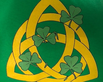 Op de afbeelding: Een groen T-shirt met een geel Keltisch knoopontwerp en vier groene klavers.