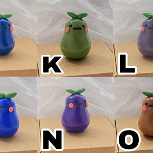 May include: Ten hand-painted ceramic figurines shaped like pears with different colors and facial expressions. The figurines are arranged in two rows of five, each on a small brown square base.