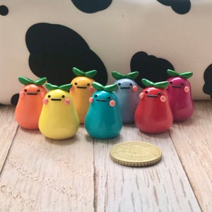 May include: Eight small, colorful, pear-shaped figurines with painted faces and green leaves on top. The figurines are arranged in a row on a light wood surface.