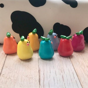 May include: A collection of eight small, hand-crafted pear-shaped figurines made of polymer clay. The figurines are painted in a rainbow of colors, including yellow, orange, red, pink, blue, green, and purple. Each figurine has a small green leaf on top and a simple, hand-painted face.