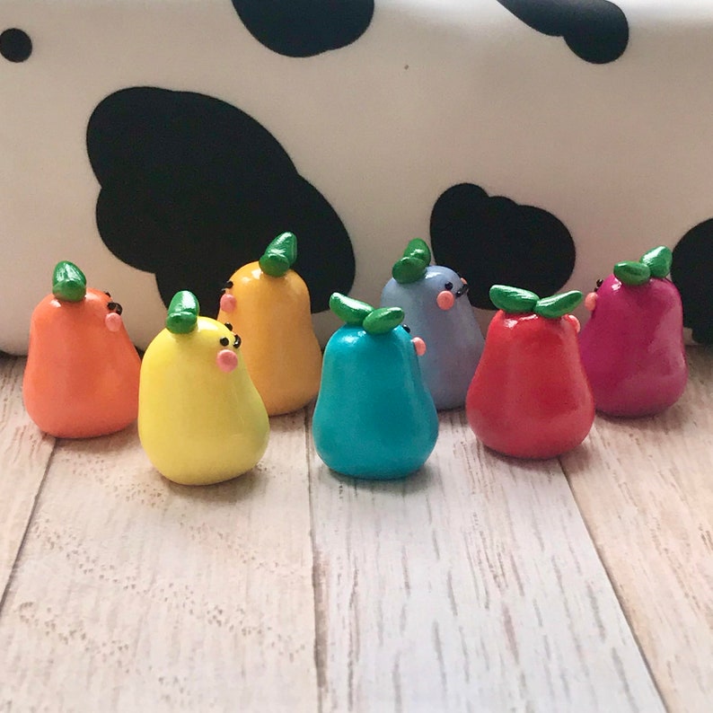 May include: A collection of eight small, hand-crafted pear-shaped figurines made of polymer clay. The figurines are painted in a rainbow of colors, including yellow, orange, red, pink, blue, green, and purple. Each figurine has a small green leaf on top and a simple, hand-painted face.