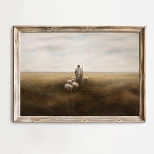 May include: Framed landscape art print depicting a shepherd and his flock in a field. The artwork features a shepherd in a white robe, guiding several sheep across a golden field under a cloudy sky. The frame is made of light-colored wood.
