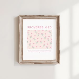 May include: A framed print with the text "PROVERBS 4:23" in pink. The print features a light pink background with a pattern of pink flowers and green leaves. The frame is a light brown colour.