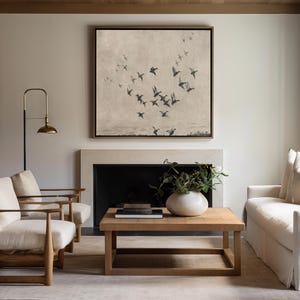 May include: A living room scene featuring a square framed artwork depicting birds in flight above a landscape. The room includes a fireplace, two armchairs, a sofa, and a wooden coffee table with a vase and books. A brass floor lamp provides additional lighting.