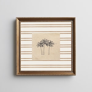 Puede incluir: Obra de arte enmarcada con un dibujo de tres palmeras. La obra de arte está sobre un lienzo beige, sobre un fondo de rayas horizontales marrones y blancas. El marco es dorado.
