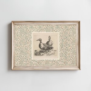 May include: Framed artwork featuring a detailed black and white etching of two ducks. The ducks are depicted in a naturalistic style. The frame is light wood with a floral patterned border in shades of green, pink, and cream.