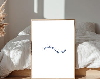 May include: A framed art print with a white background and the text "to live for the hope of it all" in a curved, navy blue font. The frame is a light wood colour. The print is displayed in a bedroom setting.