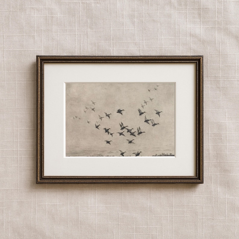 May include: Framed sepia-toned print featuring a flock of birds in flight against a muted sky. The birds are silhouetted, creating a sense of movement. The frame is a dark, ornate gold color, adding a touch of elegance to the artwork.