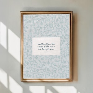 Puede incluir: Impresi&oacute;n art&iacute;stica enmarcada con un marco dorado. La impresi&oacute;n presenta un fondo floral azul claro y un rect&aacute;ngulo blanco con el texto "mightier than the waves of the sea is his love for you." El Salmo 23:4 est&aacute; impreso debajo.