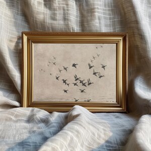 May include: A framed print featuring a flock of ducks in flight. The artwork is in muted tones of gray and brown, set against a light background. The frame is gold-colored, adding a touch of elegance to the piece.
