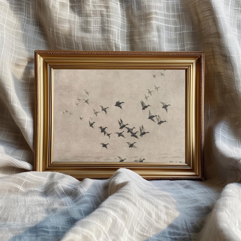 May include: A framed print featuring a flock of ducks in flight. The artwork is in muted tones of gray and brown, set against a light background. The frame is gold-colored, adding a touch of elegance to the piece.