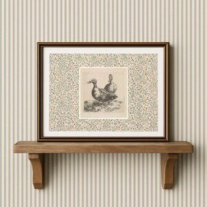 May include: A framed print featuring a detailed black and white illustration of two ducks. The artwork is set against a floral patterned background and framed in a dark brown frame. The print is displayed on a wooden shelf.