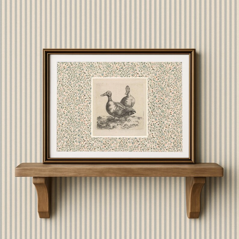 May include: A framed print featuring a detailed black and white illustration of two ducks. The artwork is set against a floral patterned background and framed in a dark brown frame. The print is displayed on a wooden shelf.