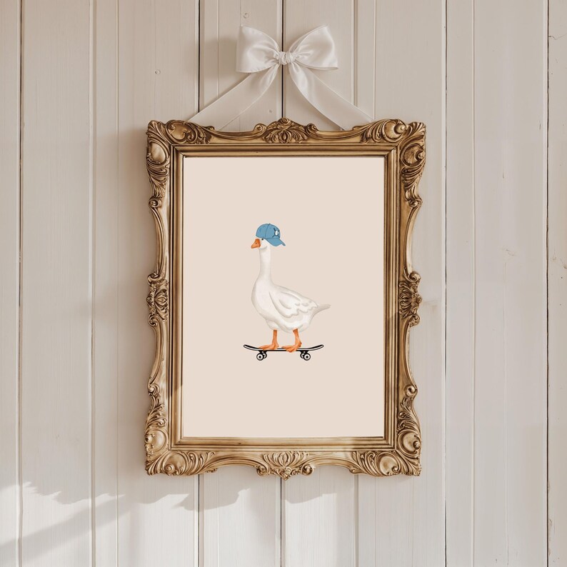 May include: A framed print featuring a white goose wearing a blue cap and riding a skateboard. The artwork is set against a beige background and framed in an ornate gold frame, with a white bow at the top.