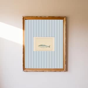 May include: A framed print of a fish illustration. The artwork is set against a blue and white striped background, within a gold-toned wooden frame. The artwork is mounted on a wall.