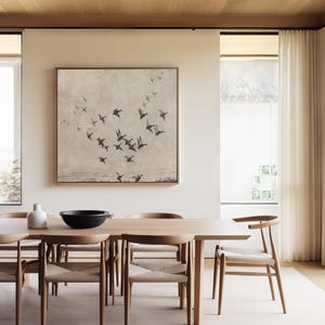 May include: A dining room featuring a large wooden table with six chairs. A framed artwork depicting a flock of birds in flight hangs above the table. A white vase and a black bowl are on the table. The room has large windows and light-colored curtains.