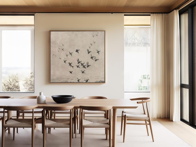 May include: A dining room featuring a large wooden table with six chairs. A framed artwork depicting a flock of birds in flight hangs above the table. A white vase and a black bowl are on the table. The room has large windows and light-colored curtains.