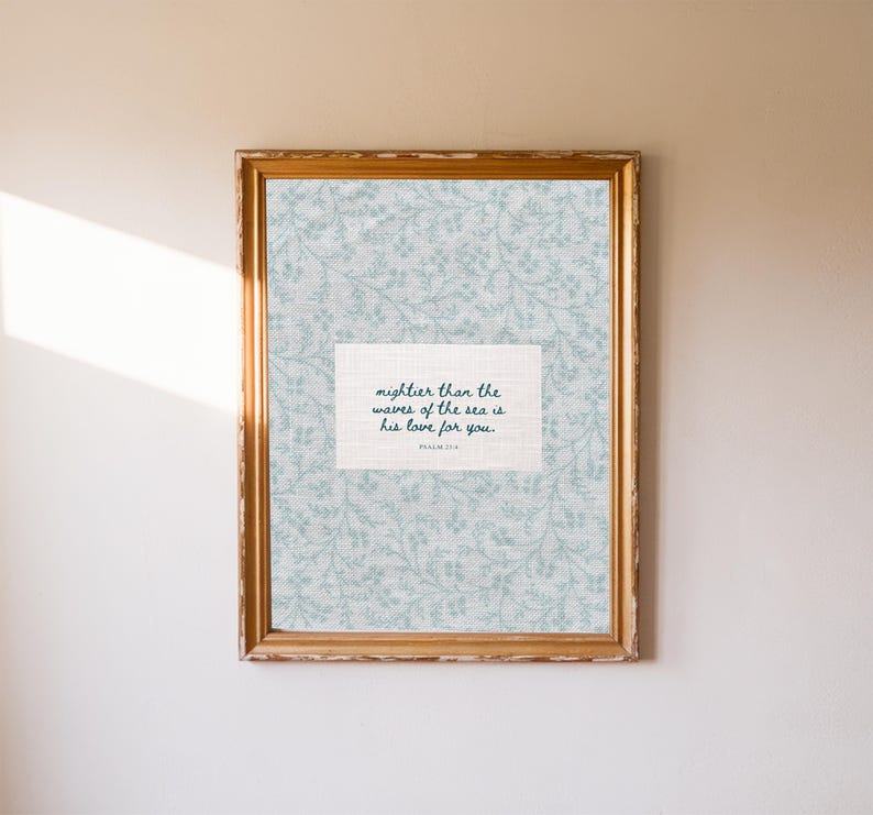 Puede incluir: Una impresi&oacute;n enmarcada con un marco dorado. La impresi&oacute;n presenta un fondo floral azul claro y un espacio rectangular blanco con el texto "mightier than the waves of the sea is his love for you."