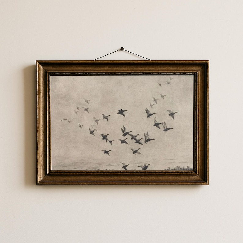 May include: A framed print featuring a flock of birds in flight against a muted, sepia-toned background. The birds are depicted in silhouette, creating a sense of movement. The frame is a dark, ornate gold color.