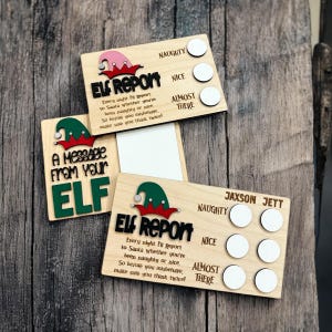 May include: Two wooden Elf Report cards with a message from the elf. The cards have a checklist for naughty or nice with a space for a name. The cards are made of light wood with a green elf hat and red and white elf shoes.