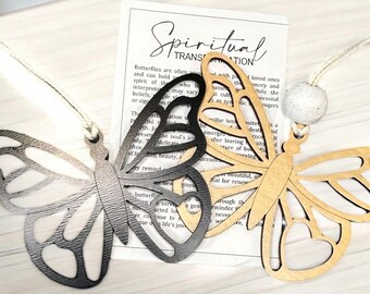 May include: Two wooden butterfly ornaments, one black and one brown, with a white bead and string. The butterflies are hanging from a white surface. The text on the card reads "Spiritual Transformation". Butterflies are often associated with passed loved ones and can hold the spirit of those who have passed. The interpretation may vary across cultures while the personal beliefs, spiritual transformation, or significance of the butterfly is as symbolic as the individual interprets it. The butterfly emerges into a new life after leaving the cocoon. It is a reminder of beauty, and a potential for renewal.