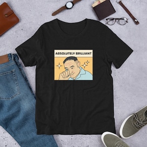 Puede incluir: Camiseta negra con una imagen de dibujos animados de un hombre con una expresión de sorpresa. El texto "ABSOLUTELY BRILLIANT" está por encima de la imagen.