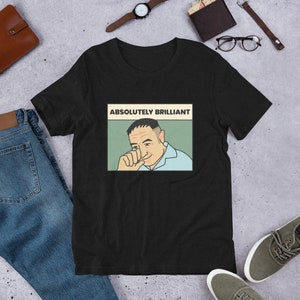 Puede incluir: Camiseta negra con una imagen de estilo pop art de un hombre y el texto "ABSOLUTAMENTE BRILLANTE". El gráfico está en un marco rectangular con un fondo verde claro. El hombre lleva una camisa azul claro.