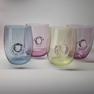 May include: Four glass tumblers with a bubble in the bottom. The tumblers are in shades of purple, blue, green, and yellow.