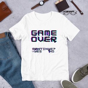 May include: White t-shirt with a black graphic that says "GAME OVER" with a glitch effect. Below the text is "CONTINUE? YES NO" with a glitch effect.
