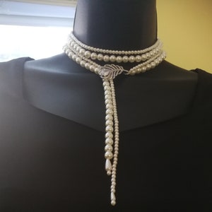 May include: A long, multi-strand pearl necklace with a decorative leaf-shaped pendant. The necklace is white and has a classic design.