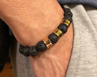 May include: A black lava rock bracelet with gold beads that have the names "John", "Eli", and "Iso" engraved on them.