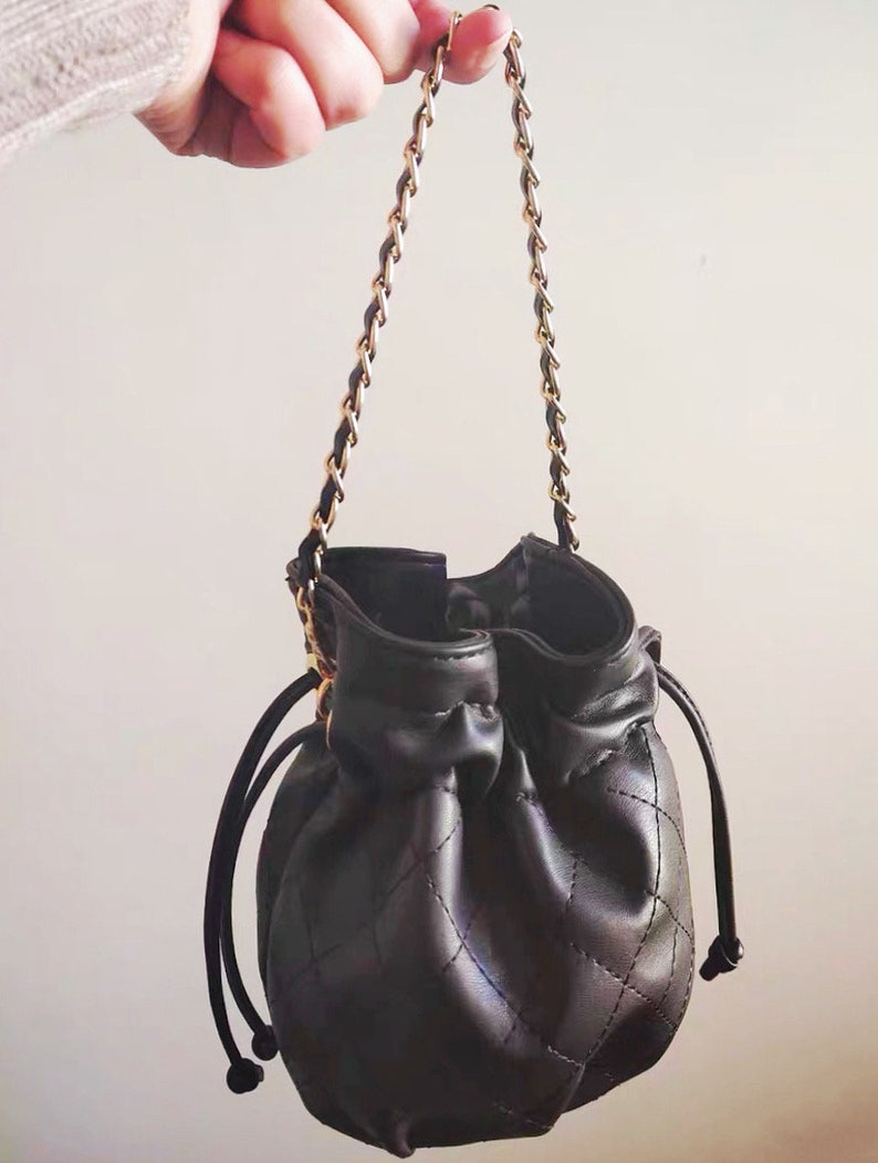 Op de afbeelding: Een zwarte quilted bucket bag met een gouden kettingband en een trekkoord.