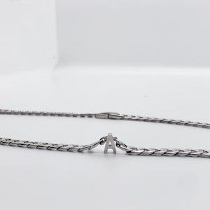 May include: A silver chain necklace with a silver letter 'A' charm.