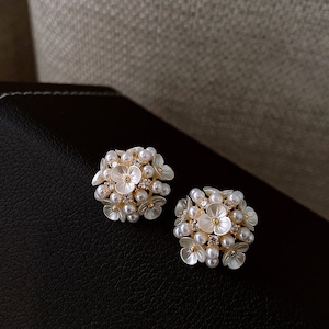 May include: A pair of gold tone earrings with white pearl and rhinestone accents. The earrings are shaped like a cluster of flowers.