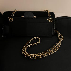 May include: A black leather wallet with a gold chain strap. The wallet has a zipper closure and a flap with a gold clasp.