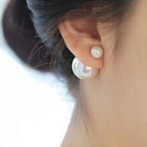 May include: A pair of white pearl earrings with a double-sided design. The earrings are worn in the earlobe.