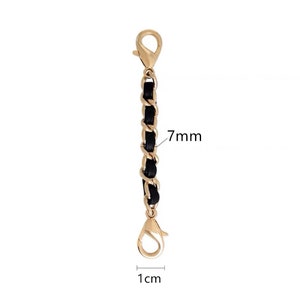 Op de afbeelding: Een gouden ketting met zwarte lederen accenten, 7 mm breed en 1 cm lang. De ketting heeft twee karabijnhaken.