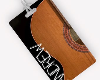 Pode incluir: Uma etiqueta de bagagem com fundo preto e o nome "ANDREW" em texto branco. A etiqueta apresenta uma imagem de perto da parte de trás de um violão acústico com acabamento em madeira natural.