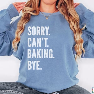 May include: A light blue sweatshirt with the text "SORRY. CAN'T. BAKING. BYE." printed in white.
