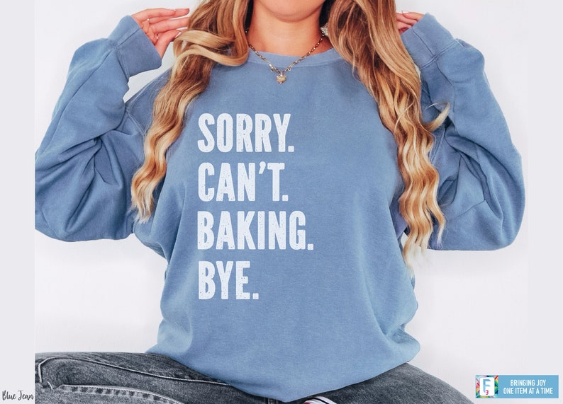 May include: A light blue sweatshirt with the text "SORRY. CAN'T. BAKING. BYE." printed in white.