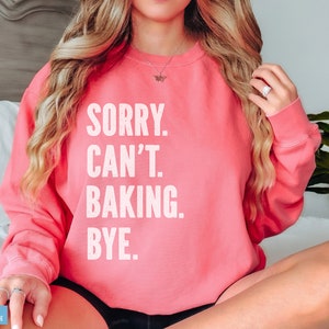 May include: A pink sweatshirt with the text "SORRY. CAN'T. BAKING. BYE." in white.